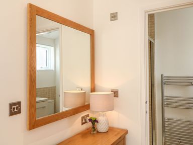 A wooden framed mirror above a wooden table with a pineapple lamp and small flower vase in a bathroom at 14 Faraway Fields in Dobwalls
