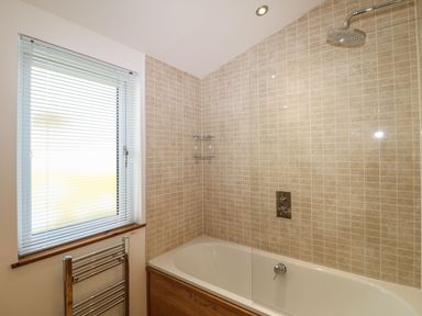 A bathroom with a bathtub shower combination under a window with blinds at 14 Faraway Fields in Dobwalls