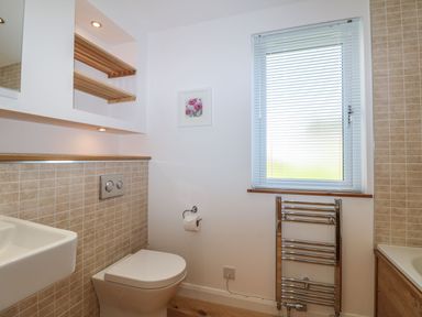 A bathroom with a toilet, a sink, a window with blinds, a heated towel rail, tiled walls, and wooden shelves at 14 Faraway Fields in Dobwalls