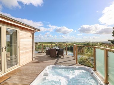 An outdoor wooden deck with a hot tub dining table and chairs overlooking fields at 14 Faraway Fields in Dobwalls