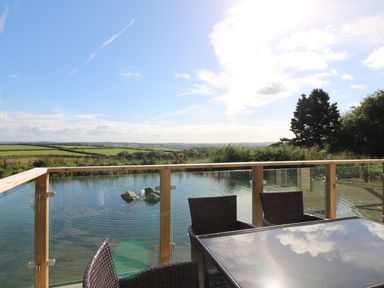 A patio table and chairs next to a glass railing overlooking a pond and fields at 14 Faraway Fields in Dobwalls