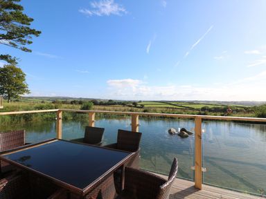 An outdoor deck with a glass table and wicker chairs overlooking a small pond and farmland at 14 Faraway Fields in Dobwalls