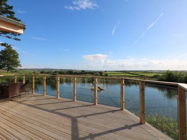 An outdoor wooden deck with glass railing overlooking a pond and green fields at 14 Faraway Fields in Dobwalls