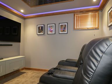 A room with leather recliner chairs a wall mounted television framed pictures and a window with blinds at 9 Meadow Retreat in Dobwalls