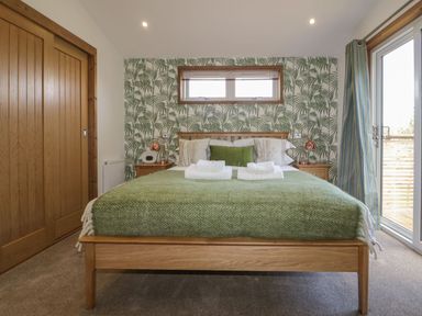 A bedroom with a wooden bed green blanket bedside tables lamps and sliding doors at 9 Meadow Retreat in Dobwalls