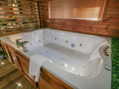 A white jacuzzi tub with chrome faucets and controls in a wooden room with window blinds and a towel hanging on the edge at 9 Meadow Retreat in Dobwalls
