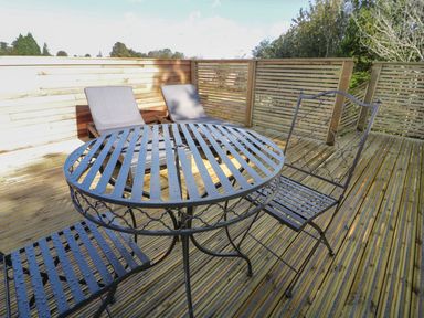 A wooden deck with a metal round table and two metal chairs and two cushioned loungers at 9 Meadow Retreat in Dobwalls