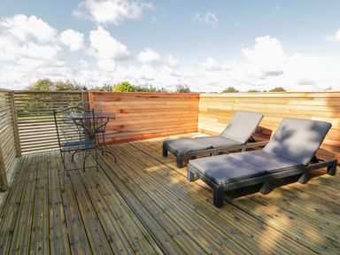 An outdoor wooden deck with two lounge chairs and a small metal table with two chairs at 9 Meadow Retreat in Dobwalls