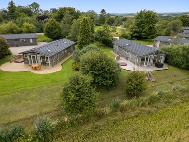 Two modern single-story houses with wooden decks and outdoor furniture surrounded by trees and grass at 9 Meadow Retreat in Dobwalls