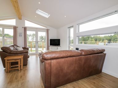 A living room with brown leather sofas wooden nesting tables and a television at 7 Meadow Retreat in Dobwalls