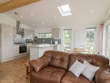 An open kitchen and dining area with a brown sofa in the foreground at 7 Meadow Retreat in Dobwalls
