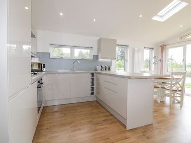 A kitchen with white cabinets wooden floor and a dining table with chairs at 7 Meadow Retreat in Dobwalls