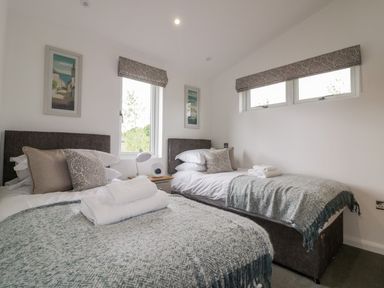 A bedroom with two single beds with gray headboards and teal throws at 7 Meadow Retreat in Dobwalls