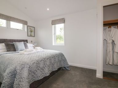 A bedroom with a bed covered with a patterned bedspread and pillows two windows a picture on the wall and an open closet with bathrobes at 7 Meadow Retreat in Dobwalls