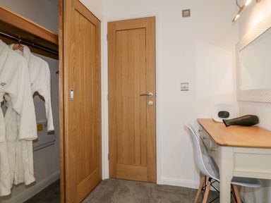 A room with a wooden door and closet doors with white robes inside a desk with a mirror and chair at 7 Meadow Retreat in Dobwalls