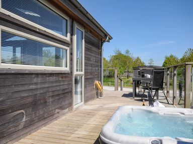 An outdoor wooden deck with a hot tub and a table with chairs at 7 Meadow Retreat in Dobwalls