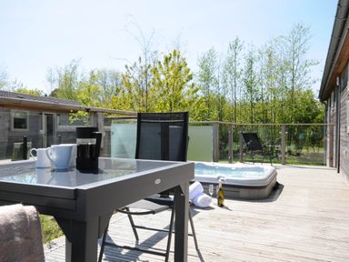 A wooden deck with a glass table, chairs, a hot tub, towels, and a bottle of champagne at 7 Meadow Retreat in Dobwalls