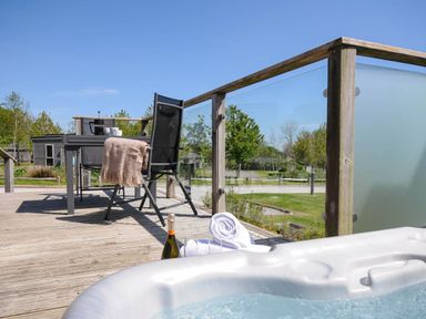 An outdoor deck with a hot tub a table and chair with a blanket and a bottle on the wooden deck at 7 Meadow Retreat in Dobwalls