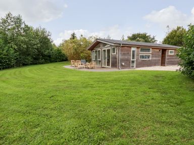 A wooden house with a patio and outdoor furniture on a large grassy lawn surrounded by trees at 14 Horizon View in Dobwalls