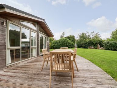 An outdoor wooden deck with a wooden table and chairs next to a house with large windows and green grass surrounded by trees and bushes at 14 Horizon View in Dobwalls
