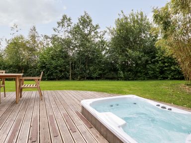 An outdoor wooden deck with a hot tub and wooden chairs next to a lawn with trees at 14 Horizon View in Dobwalls
