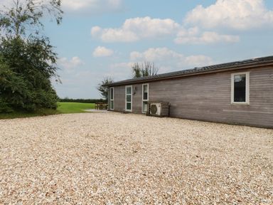 A gravel driveway leading to a single-story wooden house with doors and windows and a wooden outdoor table and chairs on a grassy area at 9 Horizon View in Dobwalls