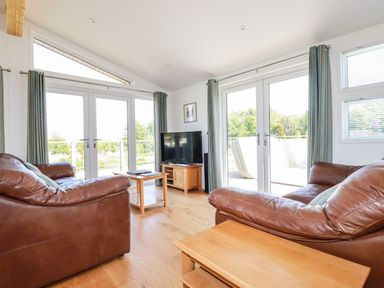 A living room with two brown leather sofas facing a TV and large glass doors at 5 Meadow Retreat in Dobwalls