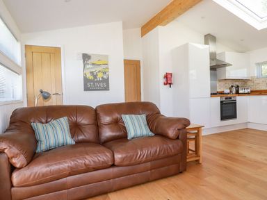 A brown leather sofa with striped pillows and a kitchen with white cabinets and wooden floors at 5 Meadow Retreat in Dobwalls