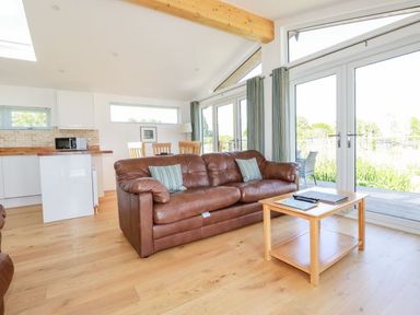 A living room with a brown sofa a wooden coffee table and large glass doors at 5 Meadow Retreat in Dobwalls
