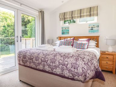 A bedroom with a double bed with patterned duvet and pillows next to glass doors leading outside at 5 Meadow Retreat in Dobwalls