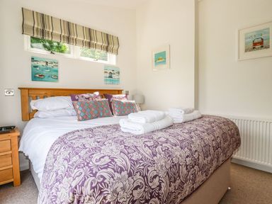 A bedroom with a wooden bed frame a bed with white sheets purple patterned blanket pillows with various patterns and folded white towels on top at 5 Meadow Retreat in Dobwalls