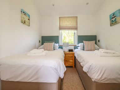 A bedroom with two single beds separated by a wooden bedside table with a lamp and a window above at 5 Meadow Retreat in Dobwalls