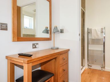 A wooden desk with a lamp and a remote control next to a mirror in a room with a towel rack and a shower at 5 Meadow Retreat in Dobwalls