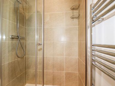 A shower stall with beige tiled walls a handheld showerhead and a metal towel rack at 5 Meadow Retreat in Dobwalls