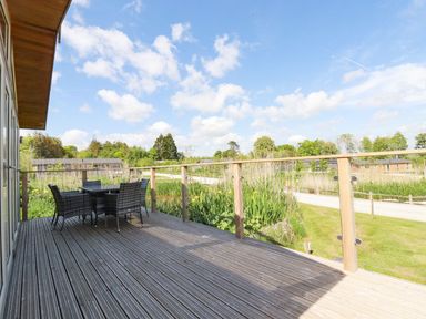 An outdoor wooden deck with a table and six chairs and a view of greenery and other buildings at 5 Meadow Retreat in Dobwalls