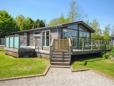 A wooden house with glass railings on a deck and a gravel pathway leading to stairs at 5 Meadow Retreat in Dobwalls