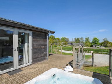 An outdoor wooden deck with a hot tub towels and wine bottle near a building at 5 Meadow Retreat in Dobwalls