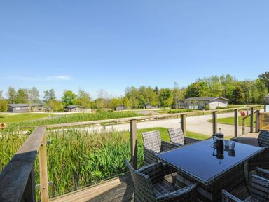 An outdoor deck with a glass table and wicker chairs overlooking greenery and several single-story buildings at 5 Meadow Retreat in Dobwalls