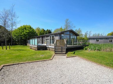 A wooden cabin with glass railings and stairs surrounded by grass and trees at 5 Meadow Retreat in Dobwalls