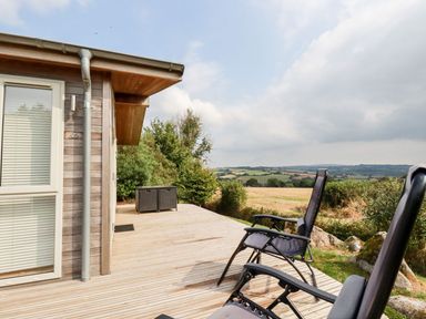 An outdoor wooden deck with two reclining chairs and storage boxes overlooking fields and hills at 11 Horizon View in Dobwalls
