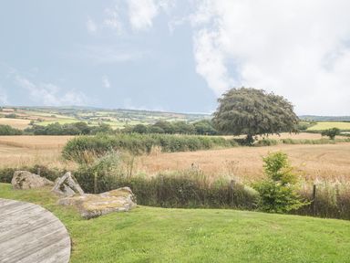 A grassy garden area with rocks and a wooden deck overlooking fields and a tree at 11 Horizon View in Dobwalls