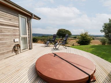 A wooden deck with two black reclining chairs and a covered circular hot tub next to a house in Dobwalls