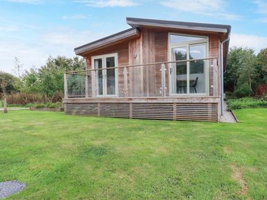A wooden cabin with glass doors and a glass railing on a grassy lawn at 2 Meadow Retreat in Dobwalls