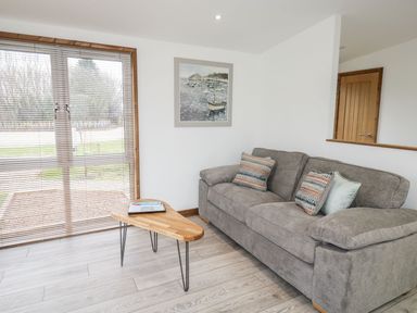 A living room with a grey sofa and wooden coffee table near window blinds at 2 Meadow Retreat in Dobwalls