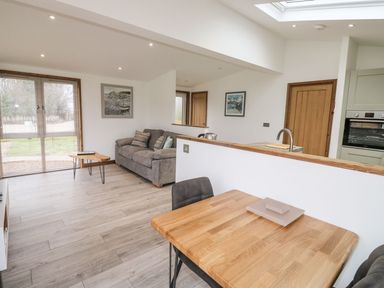 An open living and dining area with a gray sofa and wooden dining table at 2 Meadow Retreat in Dobwalls
