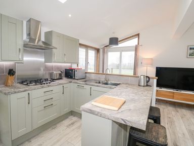 A kitchen with gray cabinets and marble countertops next to a living area with a television at 2 Meadow Retreat in Dobwalls