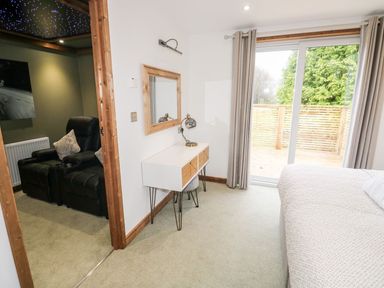 A bedroom with a bed a desk a mirror and sliding glass door next to an adjacent room with two black recliners at 2 Meadow Retreat in Dobwalls