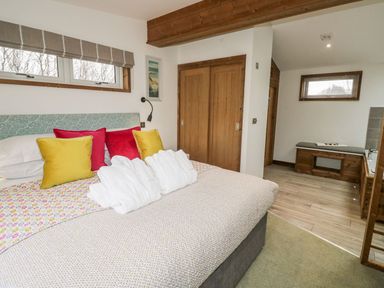 A bedroom with a bed with colorful pillows and robes with a wooden door and a bench in the adjoining room at 2 Meadow Retreat in Dobwalls