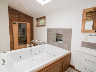A bathroom with a jacuzzi tub a wooden sauna bench and a sink with a mirror at 2 Meadow Retreat in Dobwalls