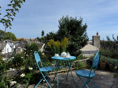 A patio with a blue metal table and two chairs with a teapot and cups surrounded by plants at 30 Sherborne Lane in Lyme Regis